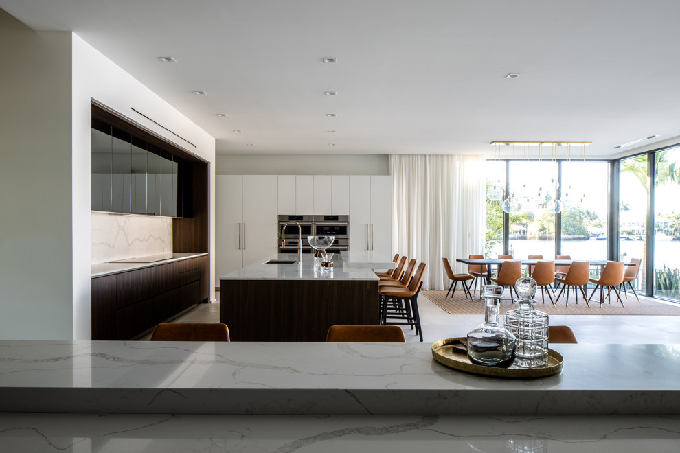 Huge minimalist l-shaped concrete floor and white floor eat-in kitchen photo in Miami with a drop-in sink, flat-panel cabinets, white cabinets, marble countertops, white backsplash, marble backsplash, paneled appliances, an island and white countertops