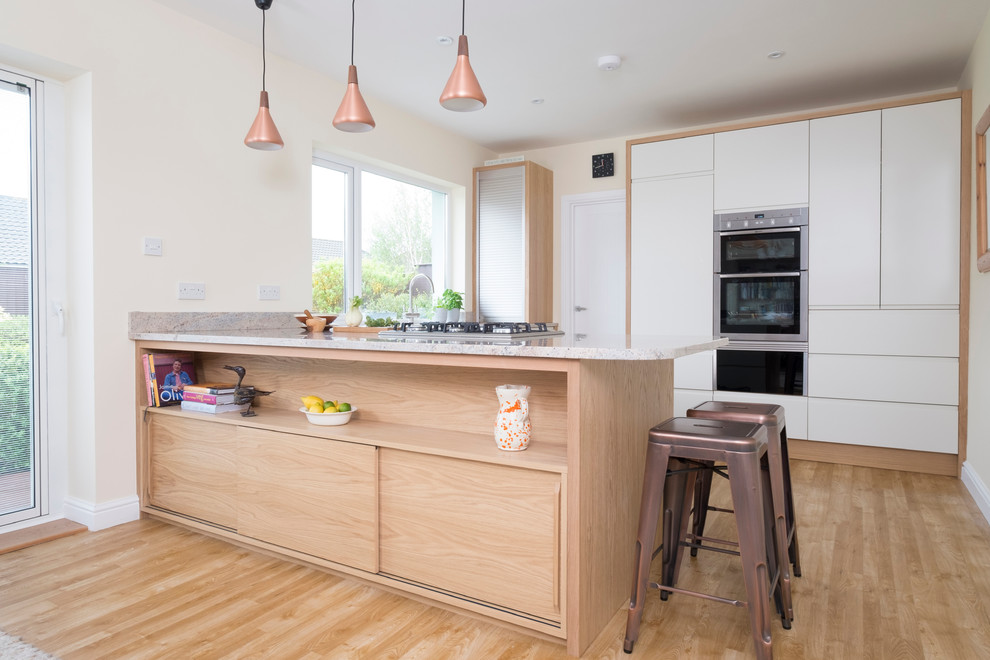 Inspiration for a mid-sized contemporary u-shaped eat-in kitchen in Cardiff with flat-panel cabinets, white cabinets, stainless steel appliances, medium hardwood floors, a peninsula, an undermount sink and granite benchtops.