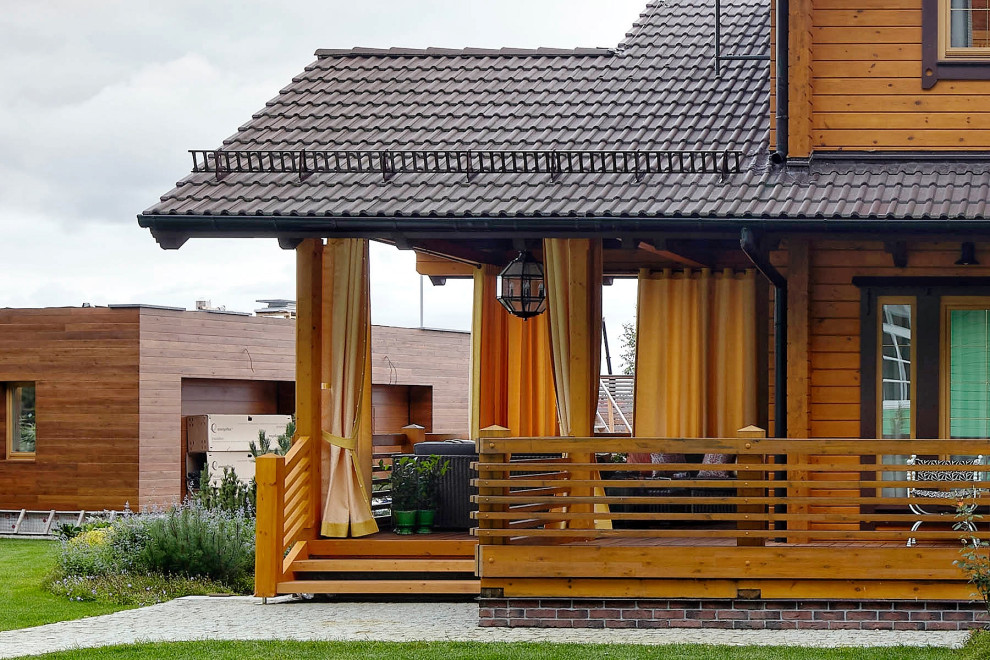 This is an example of a mid-sized country courtyard and ground level deck in Moscow with a roof extension and wood railing.