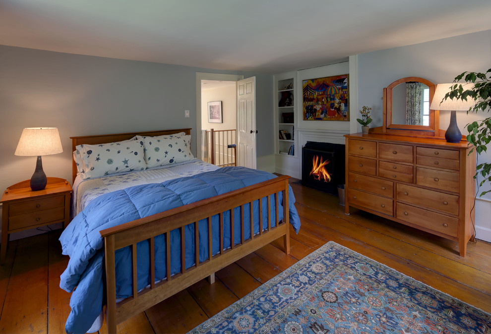 Photo of a large traditional guest bedroom in Portland Maine with blue walls, medium hardwood floors, a standard fireplace and a plaster fireplace surround.