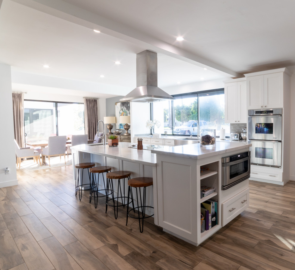 Eat-in kitchen - huge modern l-shaped eat-in kitchen idea in Phoenix with a farmhouse sink, glass-front cabinets, white cabinets, quartz countertops, gray backsplash, ceramic backsplash, stainless steel appliances, an island and white countertops