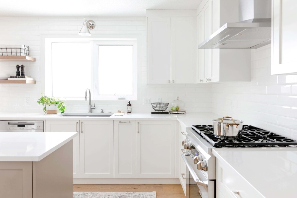 Example of a large transitional u-shaped medium tone wood floor and brown floor eat-in kitchen design in Calgary with an undermount sink, shaker cabinets, white cabinets, quartzite countertops, white backsplash, subway tile backsplash, stainless steel appliances, an island and white countertops