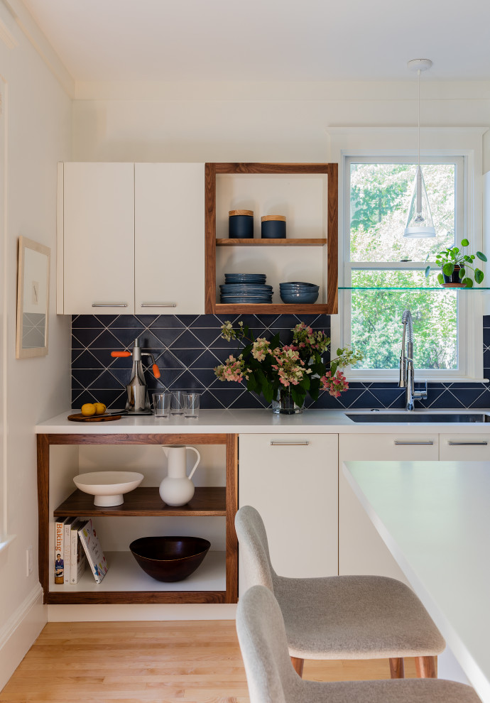 This is an example of a mid-sized contemporary l-shaped separate kitchen in Boston with an undermount sink, flat-panel cabinets, white cabinets, solid surface benchtops, blue splashback, ceramic splashback, stainless steel appliances, light hardwood floors, a peninsula and white benchtop.