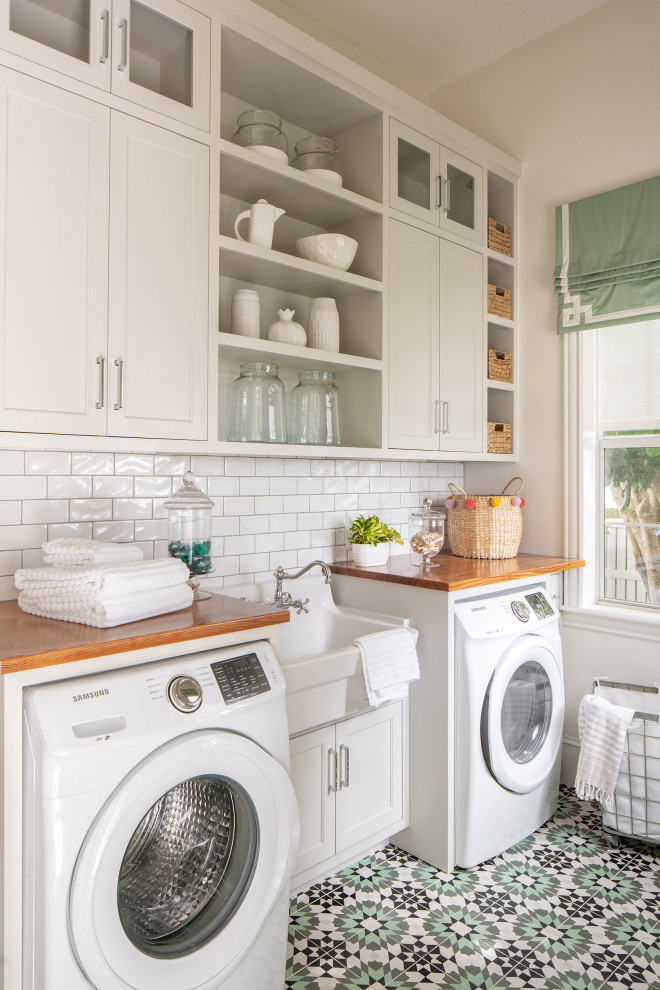 Idéer för små medelhavsstil tvättstugor enbart för tvätt, med en rustik diskho, beige skåp, träbänkskiva, vitt stänkskydd, stänkskydd i tunnelbanekakel, beige väggar, en tvättmaskin och torktumlare bredvid varandra och flerfärgat golv