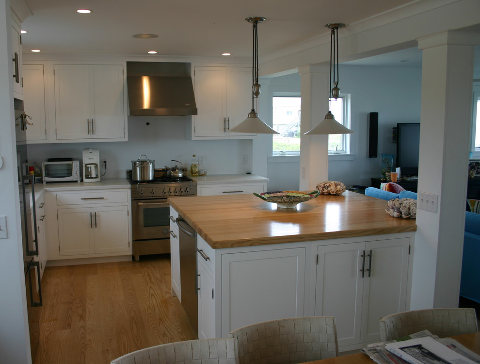 This is an example of a mid-sized beach style l-shaped open plan kitchen in Providence with an undermount sink, shaker cabinets, white cabinets, wood benchtops, stainless steel appliances, medium hardwood floors and with island.