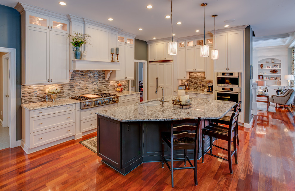 Large transitional medium tone wood floor open concept kitchen photo in Boston with a double-bowl sink, recessed-panel cabinets, white cabinets, granite countertops, multicolored backsplash, glass tile backsplash, paneled appliances and an island