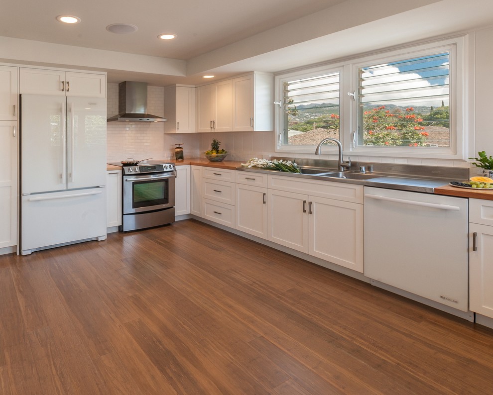 This is an example of a transitional kitchen in Hawaii with shaker cabinets, white cabinets, wood benchtops, white splashback, ceramic splashback, white appliances, bamboo floors and no island.