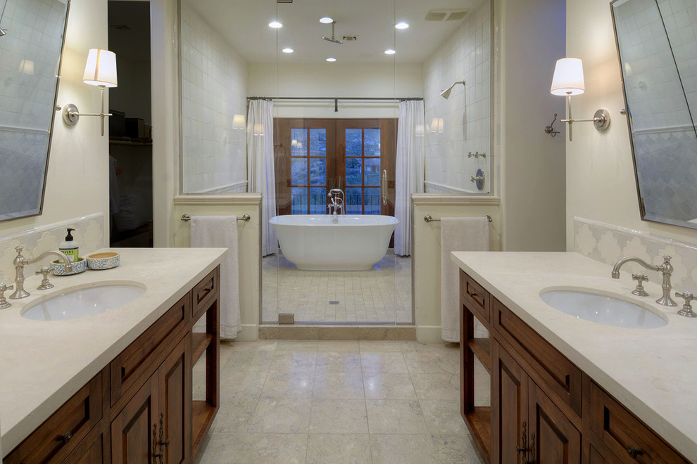 This is an example of a large mediterranean master wet room bathroom in Other with furniture-like cabinets, dark wood cabinets, a freestanding tub, beige tile, ceramic tile, beige walls, limestone floors, an undermount sink, limestone benchtops, beige floor and a hinged shower door.