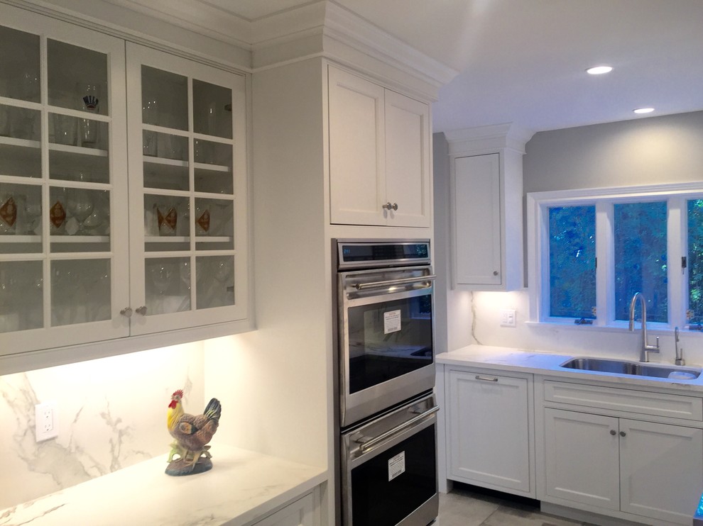 Photo of a mid-sized transitional l-shaped kitchen pantry in New York with an undermount sink, flat-panel cabinets, white cabinets, recycled glass benchtops, white splashback, glass sheet splashback, panelled appliances, dark hardwood floors and no island.