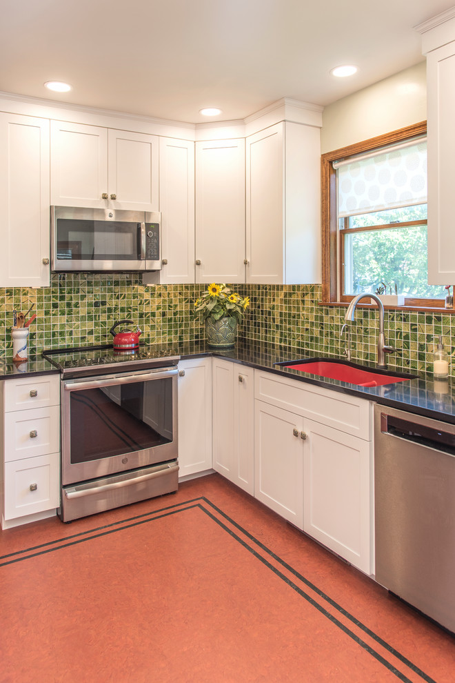 Inspiration for a mid-sized transitional l-shaped linoleum floor and red floor eat-in kitchen remodel in Philadelphia with a double-bowl sink, shaker cabinets, white cabinets, quartzite countertops, green backsplash, glass tile backsplash, stainless steel appliances and black countertops