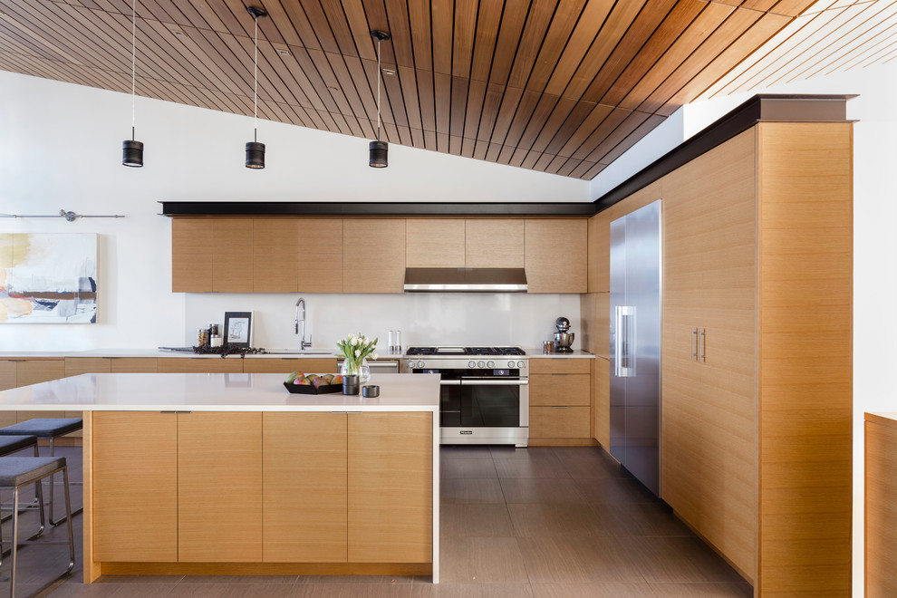 Photo of a contemporary l-shaped open plan kitchen in Seattle with an undermount sink, flat-panel cabinets, medium wood cabinets, solid surface benchtops, white splashback, stainless steel appliances, porcelain floors, with island, grey floor and white benchtop.