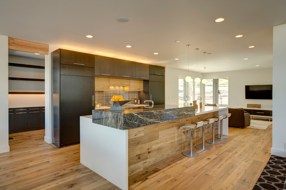 Photo of a mid-sized contemporary galley open plan kitchen in Salt Lake City with flat-panel cabinets, dark wood cabinets, grey splashback, panelled appliances, medium hardwood floors and with island.
