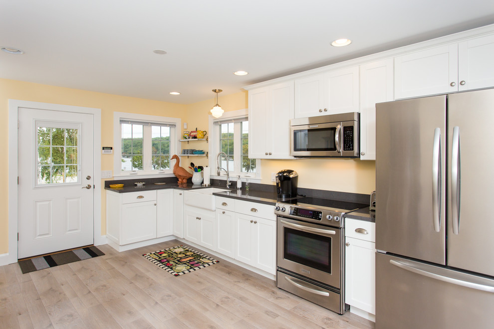 Photo of a mid-sized traditional l-shaped open plan kitchen in Boston with a farmhouse sink, shaker cabinets, white cabinets, quartz benchtops, black splashback, stone slab splashback, stainless steel appliances, painted wood floors and no island.