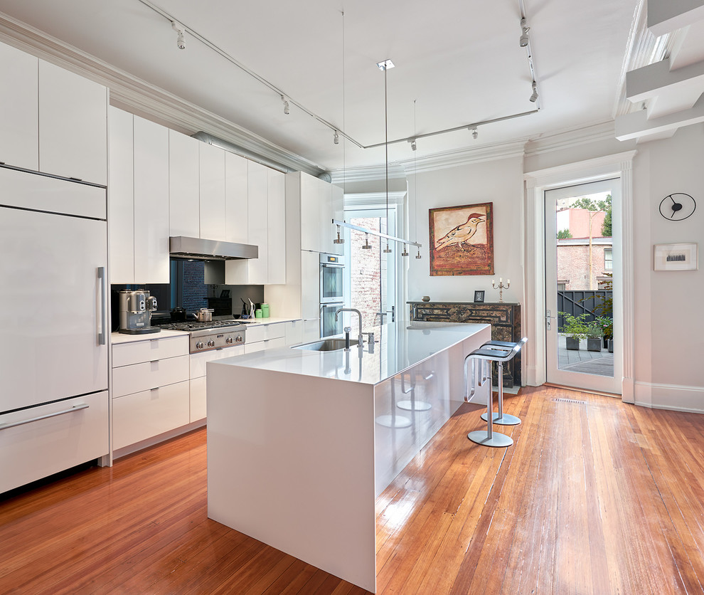 Photo of a contemporary kitchen in DC Metro with flat-panel cabinets, white cabinets, solid surface benchtops, black splashback, glass sheet splashback, medium hardwood floors, with island, a single-bowl sink and panelled appliances.