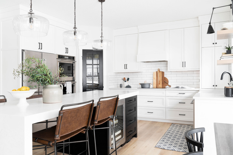 Photo of a mid-sized scandinavian u-shaped eat-in kitchen in Calgary with a farmhouse sink, shaker cabinets, white cabinets, quartz benchtops, white splashback, porcelain splashback, stainless steel appliances, with island, beige floor, white benchtop and light hardwood floors.