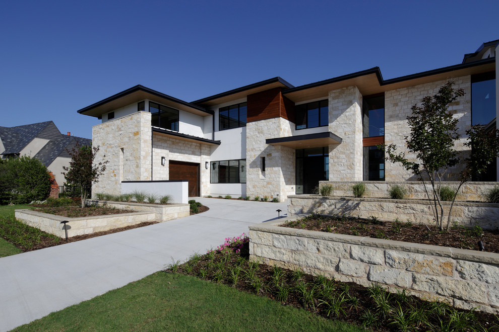 This is an example of a large modern two-storey beige exterior in Dallas with stone veneer and a flat roof.