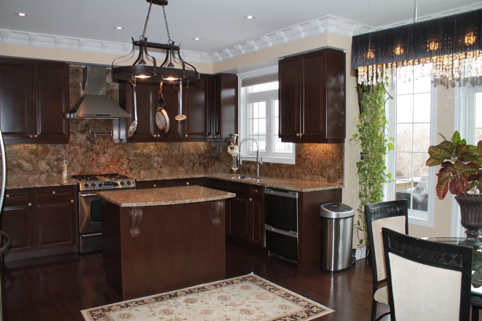 Photo of a large traditional u-shaped eat-in kitchen in Toronto with an undermount sink, raised-panel cabinets, dark wood cabinets, granite benchtops, brown splashback, stone slab splashback, stainless steel appliances, dark hardwood floors, with island, brown floor and beige benchtop.