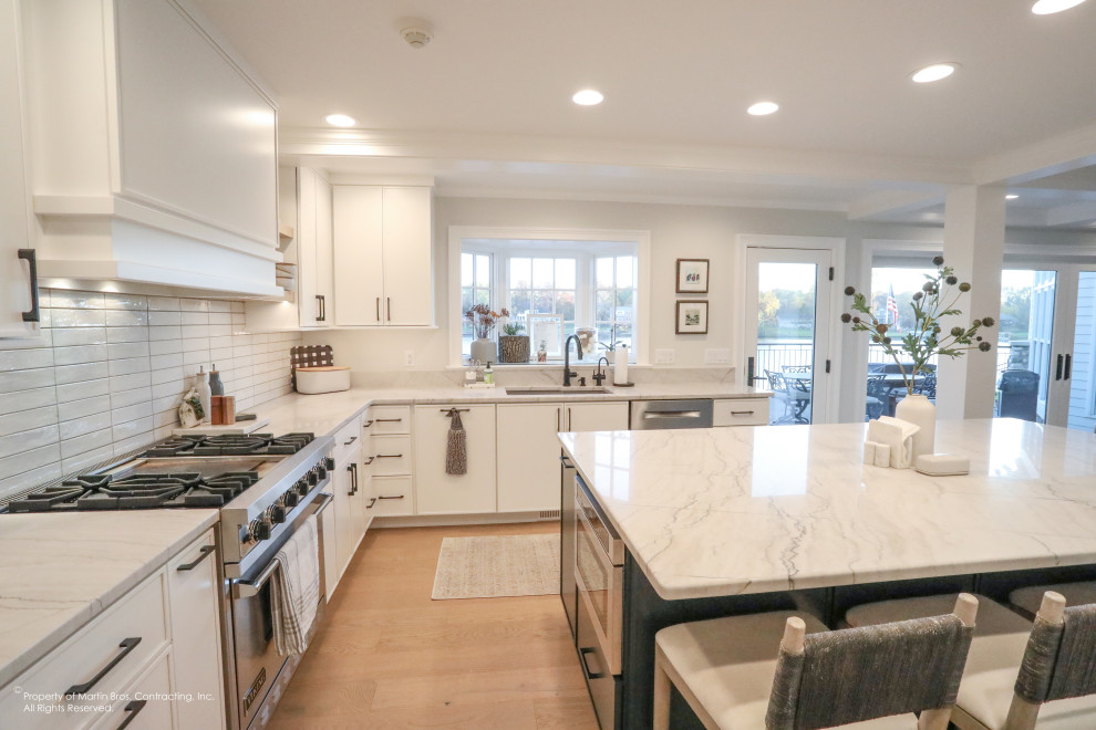 Open concept kitchen - large transitional u-shaped light wood floor open concept kitchen idea with an undermount sink, flat-panel cabinets, white cabinets, quartzite countertops, white backsplash, porcelain backsplash, stainless steel appliances, an island and white countertops