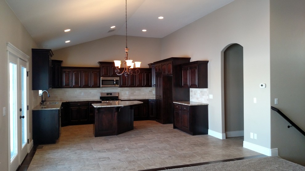 Large transitional u-shaped porcelain tile open concept kitchen photo with an undermount sink, raised-panel cabinets, dark wood cabinets, granite countertops, beige backsplash, stone tile backsplash, stainless steel appliances and an island