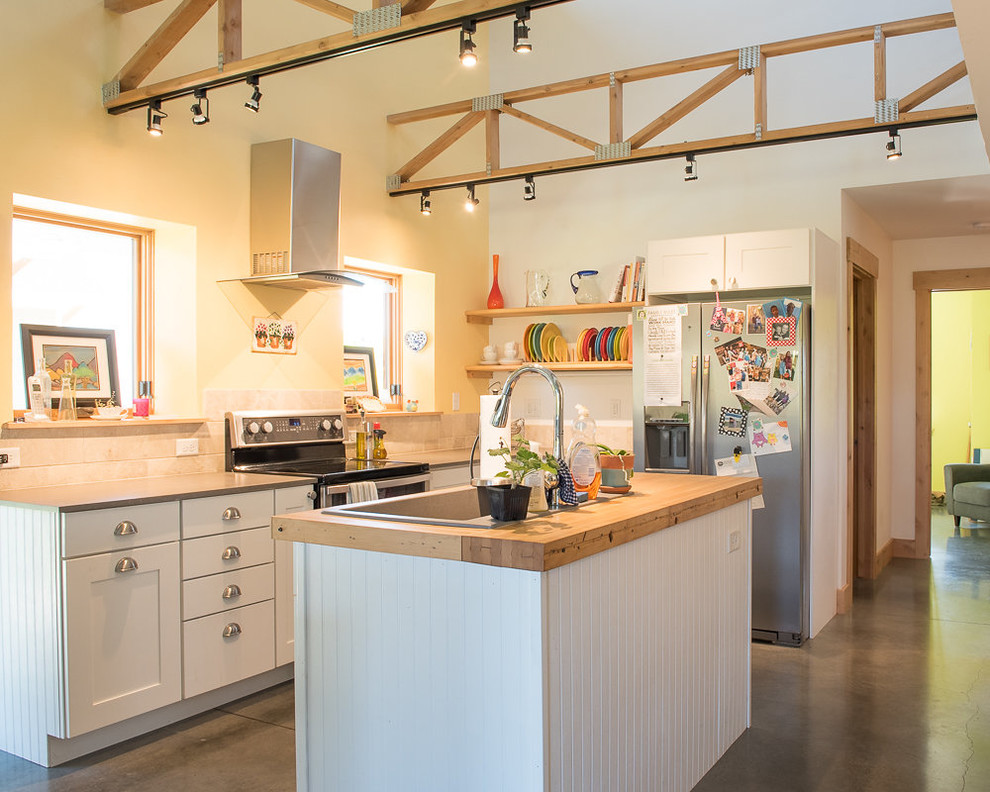 Example of a mid-sized transitional l-shaped concrete floor and gray floor open concept kitchen design with a drop-in sink, shaker cabinets, white cabinets, wood countertops, yellow backsplash, stainless steel appliances, an island and brown countertops