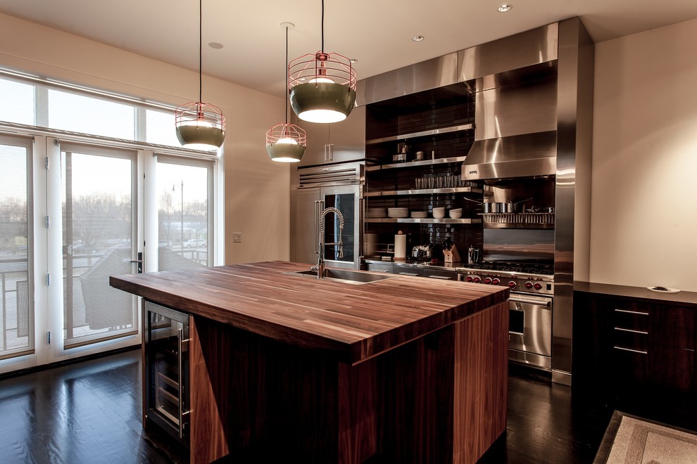 Mid-sized contemporary single-wall eat-in kitchen in Chicago with wood benchtops, stainless steel appliances, dark hardwood floors, with island, flat-panel cabinets, stainless steel cabinets, an undermount sink, grey splashback, glass tile splashback and brown floor.