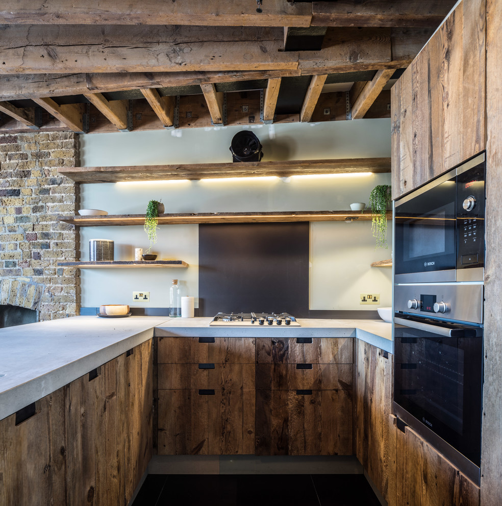 Photo of a mid-sized country u-shaped open plan kitchen in London with flat-panel cabinets, medium wood cabinets, concrete benchtops, grey splashback, stainless steel appliances, a peninsula and black floor.