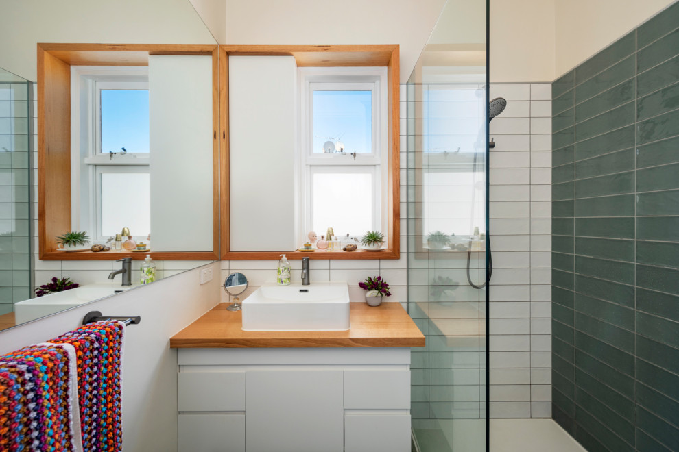 Mid-sized contemporary 3/4 bathroom in Melbourne with recessed-panel cabinets, white cabinets, an open shower, a wall-mount toilet, green tile, ceramic tile, multi-coloured walls, ceramic floors, a trough sink, wood benchtops, multi-coloured floor, an open shower, white benchtops, a single vanity and a floating vanity.