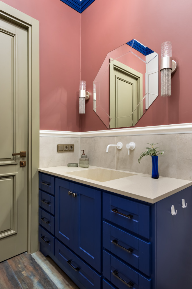 Источник вдохновения для домашнего уюта: главная ванная комната среднего размера: освещение в стиле неоклассика (современная классика) с фасадами с утопленной филенкой, синими фасадами, ванной в нише, инсталляцией, бежевой плиткой, керамогранитной плиткой, красными стенами, полом из керамогранита, монолитной раковиной, столешницей из искусственного камня, разноцветным полом, бежевой столешницей, тумбой под одну раковину и напольной тумбой