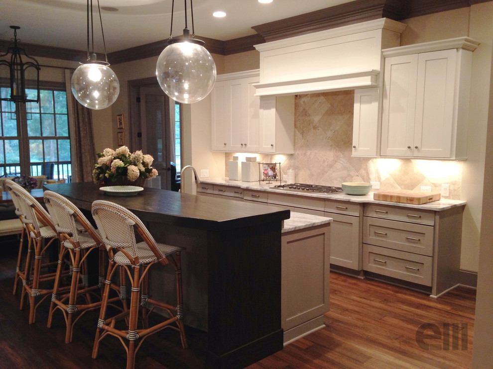 Eat-in kitchen - mid-sized transitional l-shaped medium tone wood floor eat-in kitchen idea in Charlotte with a farmhouse sink, shaker cabinets, white cabinets, marble countertops, beige backsplash, stone tile backsplash, stainless steel appliances and an island