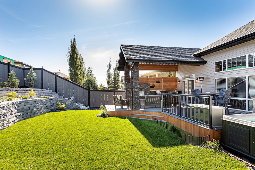 Mid-sized country backyard and ground level deck in Edmonton with with fireplace, a roof extension and glass railing.