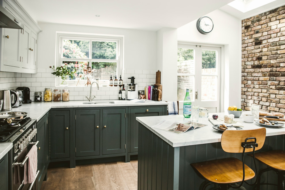 Photo of a country l-shaped eat-in kitchen in London with an undermount sink, shaker cabinets, green cabinets, white splashback, subway tile splashback, stainless steel appliances, medium hardwood floors, with island, brown floor and white benchtop.