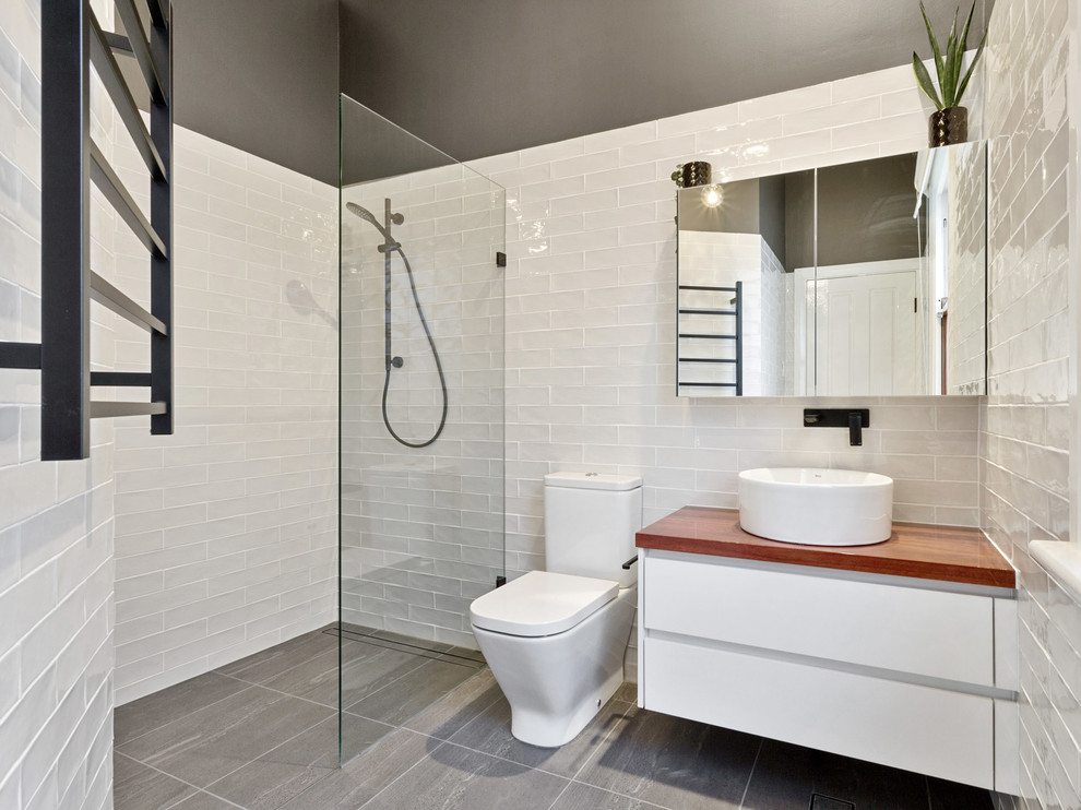 This is an example of a mid-sized contemporary master bathroom in Perth with a one-piece toilet, black and white tile, subway tile, ceramic floors, a vessel sink, wood benchtops, an open shower, white walls and black floor.