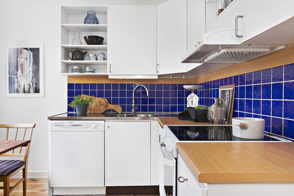 Inspiration for a small scandinavian l-shaped eat-in kitchen in Stockholm with wood benchtops, blue splashback, no island, an integrated sink, flat-panel cabinets, white cabinets, white appliances, light hardwood floors, beige floor and beige benchtop.