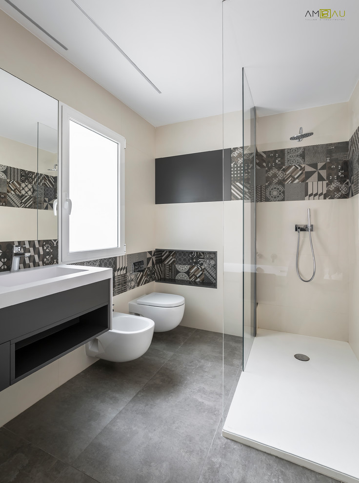 Photo of a mid-sized contemporary 3/4 bathroom in Valencia with open cabinets, grey cabinets, a corner shower, a wall-mount toilet, beige tile, black and white tile, ceramic tile, beige walls, concrete floors and a trough sink.