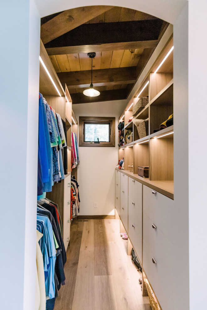 Foto di una grande cabina armadio con ante lisce, ante bianche, pavimento in legno massello medio, pavimento marrone e travi a vista