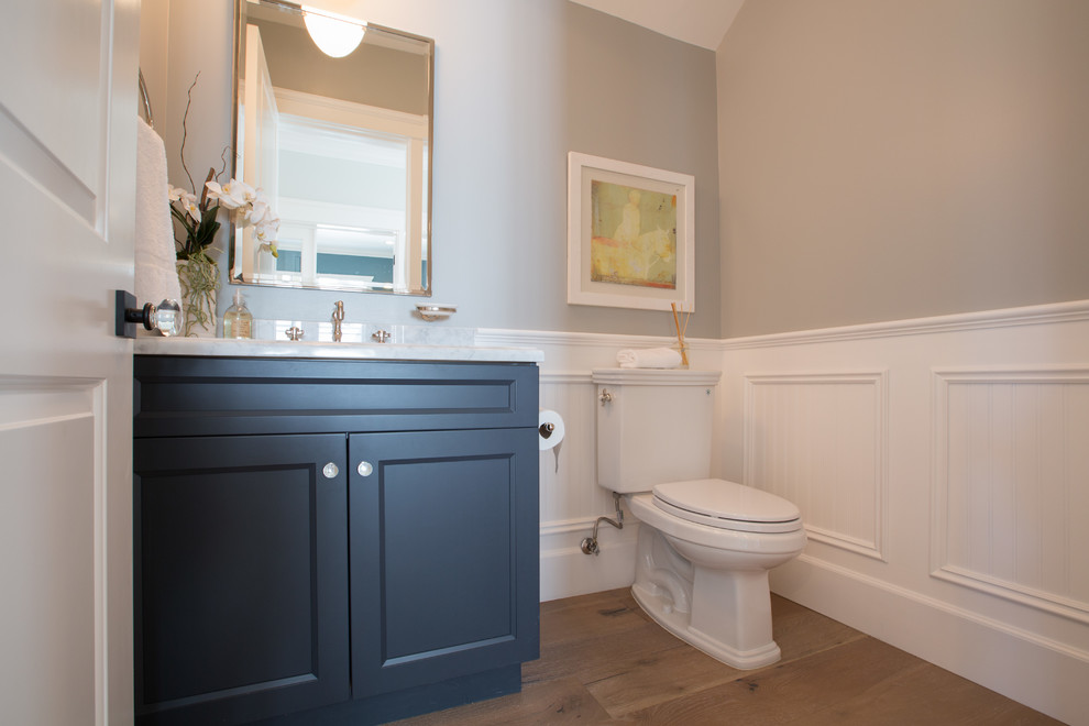 Photo of a mid-sized traditional powder room in Los Angeles with an undermount sink, recessed-panel cabinets, black cabinets, marble benchtops, a two-piece toilet, grey walls and light hardwood floors.