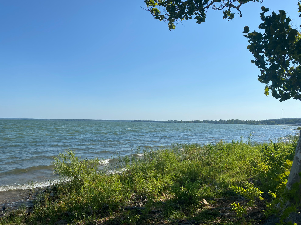rocky lakshore with trees greenery and blue sky