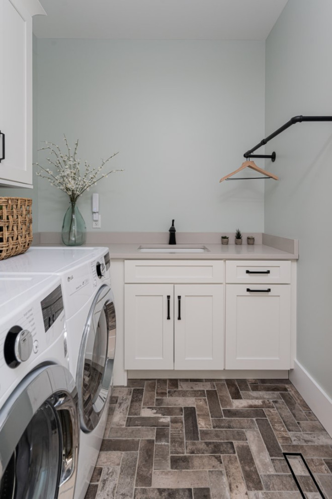Inspiration för en mellanstor grå l-formad grått tvättstuga enbart för tvätt, med en undermonterad diskho, skåp i shakerstil, vita skåp, bänkskiva i kvarts, blå väggar, tegelgolv, en tvättmaskin och torktumlare bredvid varandra och grått golv