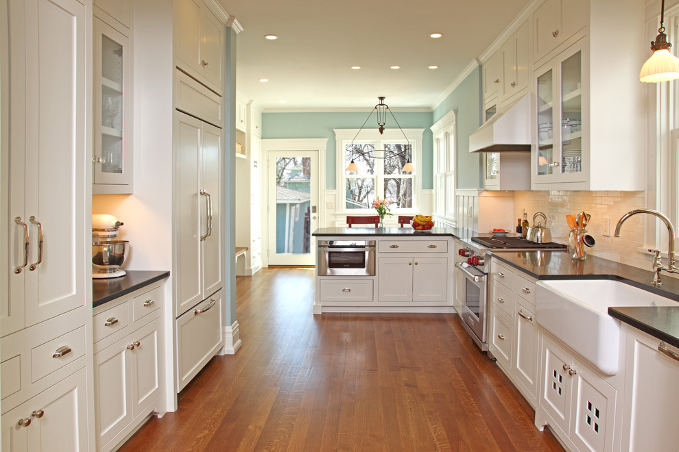 This is an example of a traditional u-shaped kitchen in Minneapolis with a farmhouse sink, shaker cabinets, white cabinets, white splashback, subway tile splashback and panelled appliances.