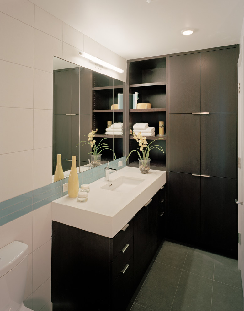 This is an example of a small modern 3/4 bathroom in San Francisco with an undermount sink, flat-panel cabinets, dark wood cabinets, solid surface benchtops, a two-piece toilet, white tile, ceramic tile, white walls, porcelain floors, an alcove tub, a shower/bathtub combo, grey floor, an open shower, white benchtops, a single vanity and wood walls.