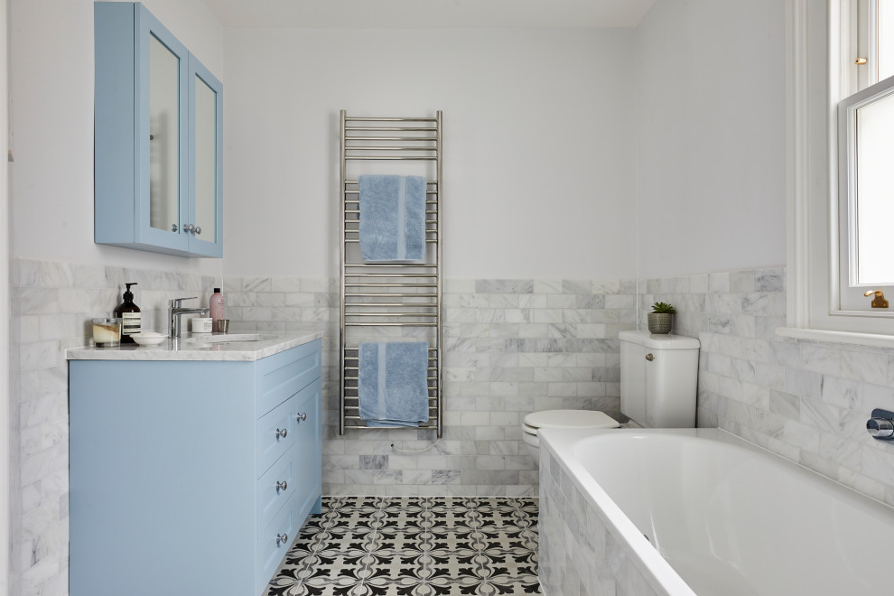 Design ideas for a large contemporary kids bathroom in London with blue cabinets, a drop-in tub, an open shower, a two-piece toilet, gray tile, an integrated sink, marble benchtops, a hinged shower door, a single vanity and a freestanding vanity.