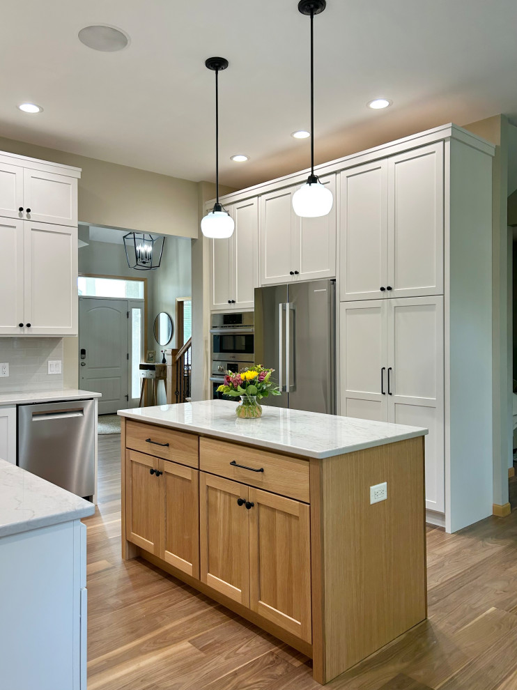 Mid-sized transitional l-shaped medium tone wood floor and brown floor open concept kitchen photo with an undermount sink, flat-panel cabinets, white cabinets, quartz countertops, gray backsplash, ceramic backsplash, stainless steel appliances, an island and white countertops