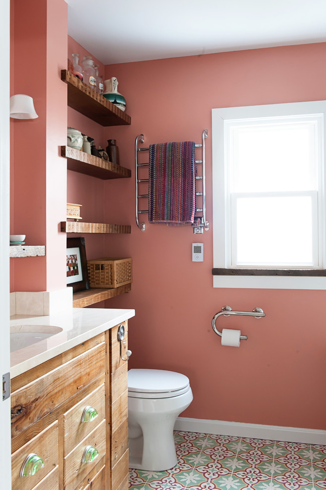 Photo of a small country 3/4 bathroom in DC Metro with an undermount sink, furniture-like cabinets, medium wood cabinets, marble benchtops, an undermount tub, a shower/bathtub combo, a two-piece toilet, white tile, ceramic tile, pink walls, concrete floors and beige benchtops.