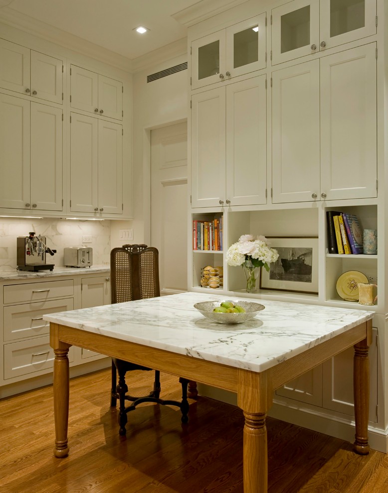This is an example of a traditional kitchen in New York with recessed-panel cabinets, white cabinets, marble benchtops, white splashback, medium hardwood floors and with island.