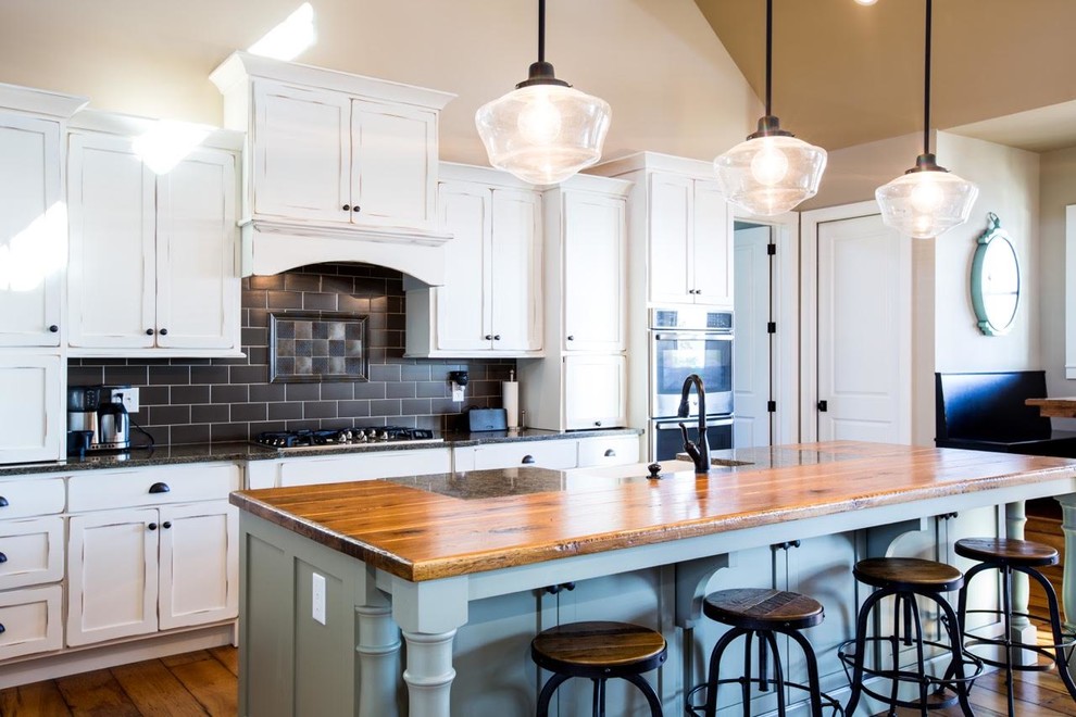 Photo of an expansive country l-shaped eat-in kitchen in Indianapolis with a farmhouse sink, shaker cabinets, distressed cabinets, wood benchtops, black splashback, metal splashback, stainless steel appliances, medium hardwood floors and with island.
