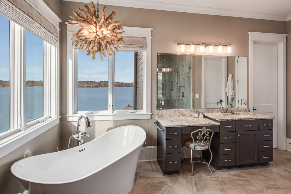 Mid-sized country master bathroom in Other with shaker cabinets, brown cabinets, a freestanding tub, an alcove shower, a one-piece toilet, gray tile, beige walls, an undermount sink, beige floor, a hinged shower door and multi-coloured benchtops.