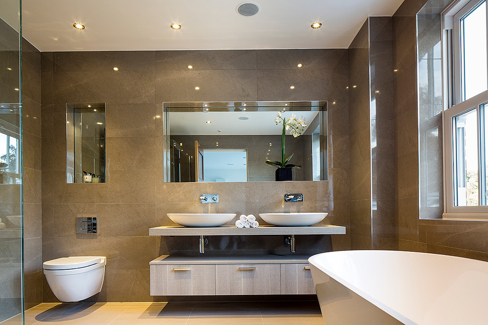 Inspiration for a large modern bathroom in London with a console sink, a freestanding tub, a wall-mount toilet, beige tile, porcelain tile, beige walls and porcelain floors.