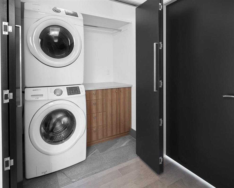 Contemporary single-wall laundry cupboard in Edmonton with flat-panel cabinets, medium wood cabinets, quartz benchtops, white walls, porcelain floors and a stacked washer and dryer.