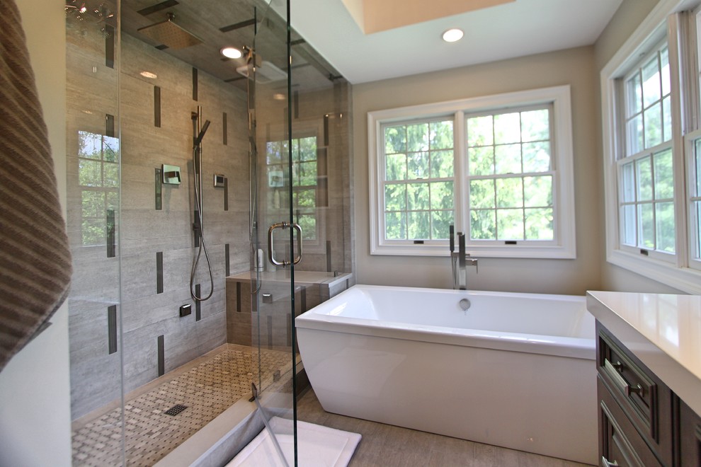 Inspiration for a large transitional master bathroom in New York with grey cabinets, a freestanding tub, an alcove shower, a one-piece toilet, gray tile, porcelain tile, grey walls, porcelain floors, an undermount sink, engineered quartz benchtops, grey floor, a hinged shower door and raised-panel cabinets.