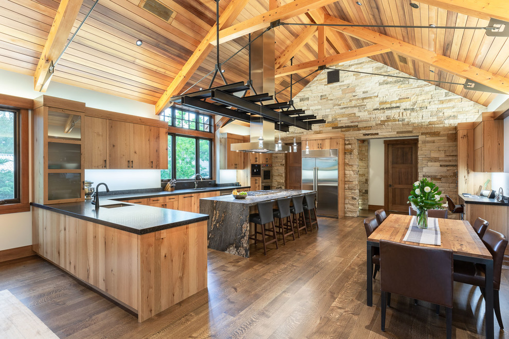 This is an example of an arts and crafts open plan kitchen in Denver with flat-panel cabinets, medium wood cabinets, stainless steel appliances, medium hardwood floors, with island, brown floor and grey benchtop.